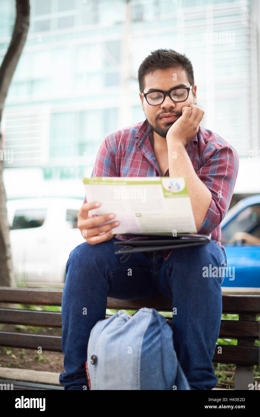 Hispanic man sitting on top of bench reading brochure Stock Photo