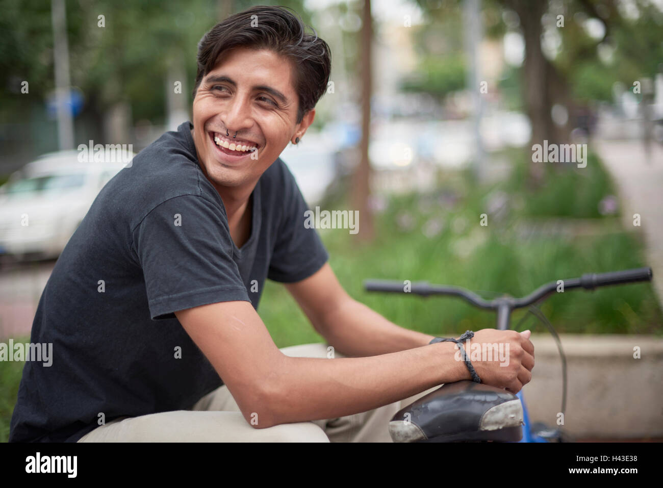 Laughing Hispanic man sitting with bicycle Stock Photo