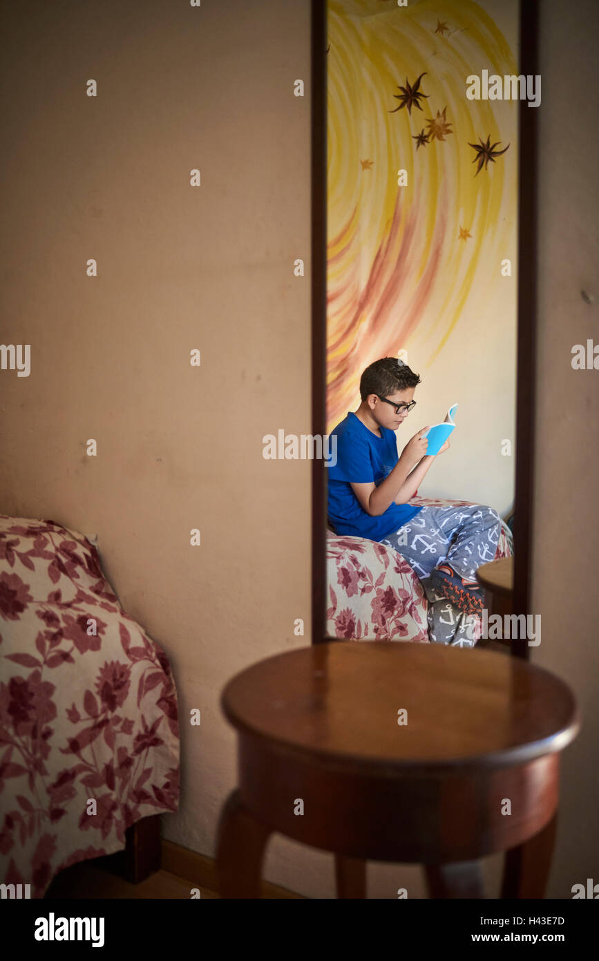 Reflection in mirror of Hispanic boy reading book on bed Stock Photo