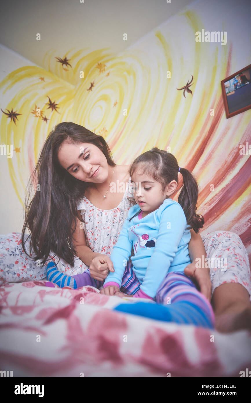 Hispanic mother and daughter on bed looking down Stock Photo