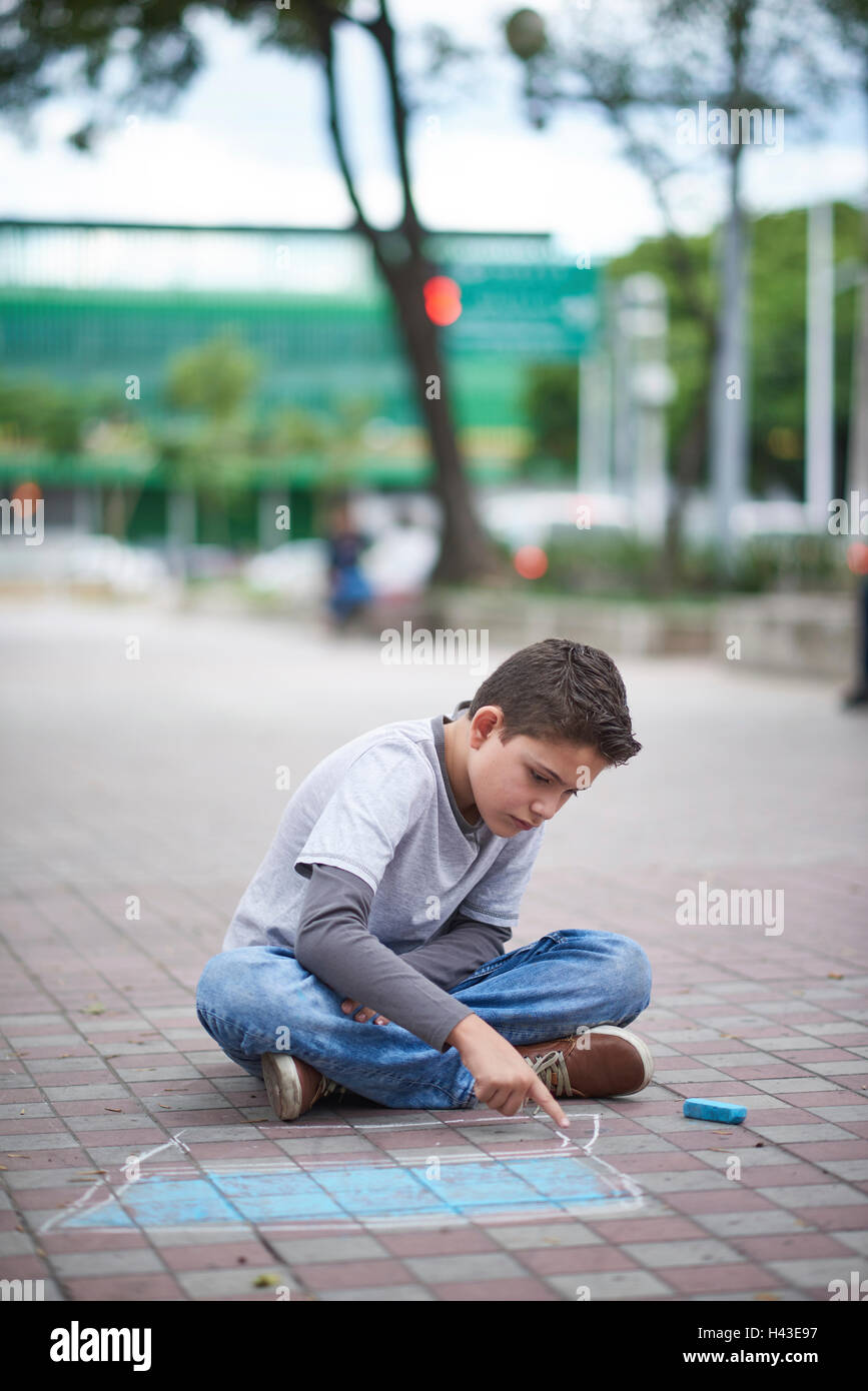 Hispanic boy drawing laptop with chalk on sidewalk Stock Photo