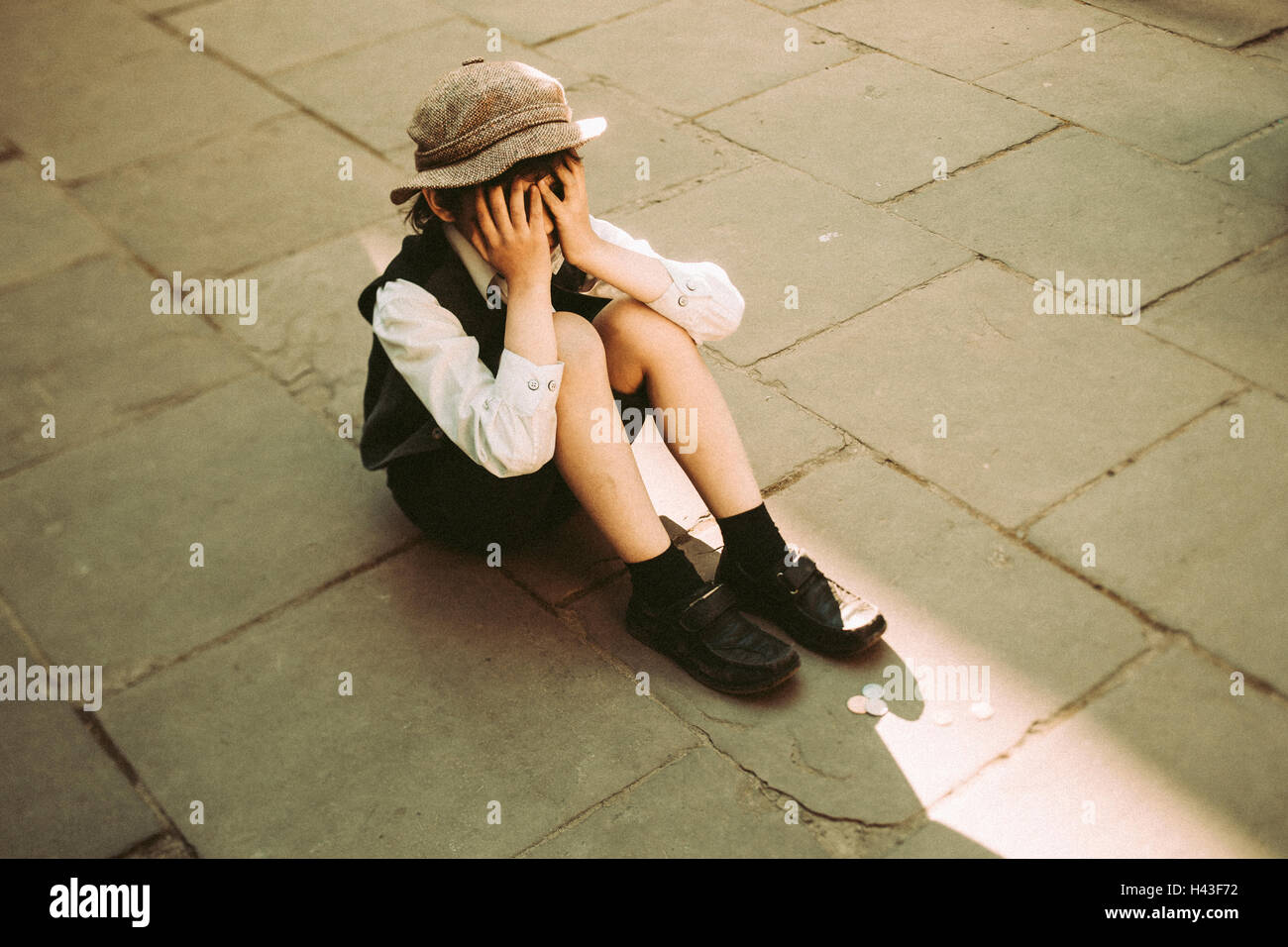 Old-fashioned Caucasian sitting in street crying Stock Photo