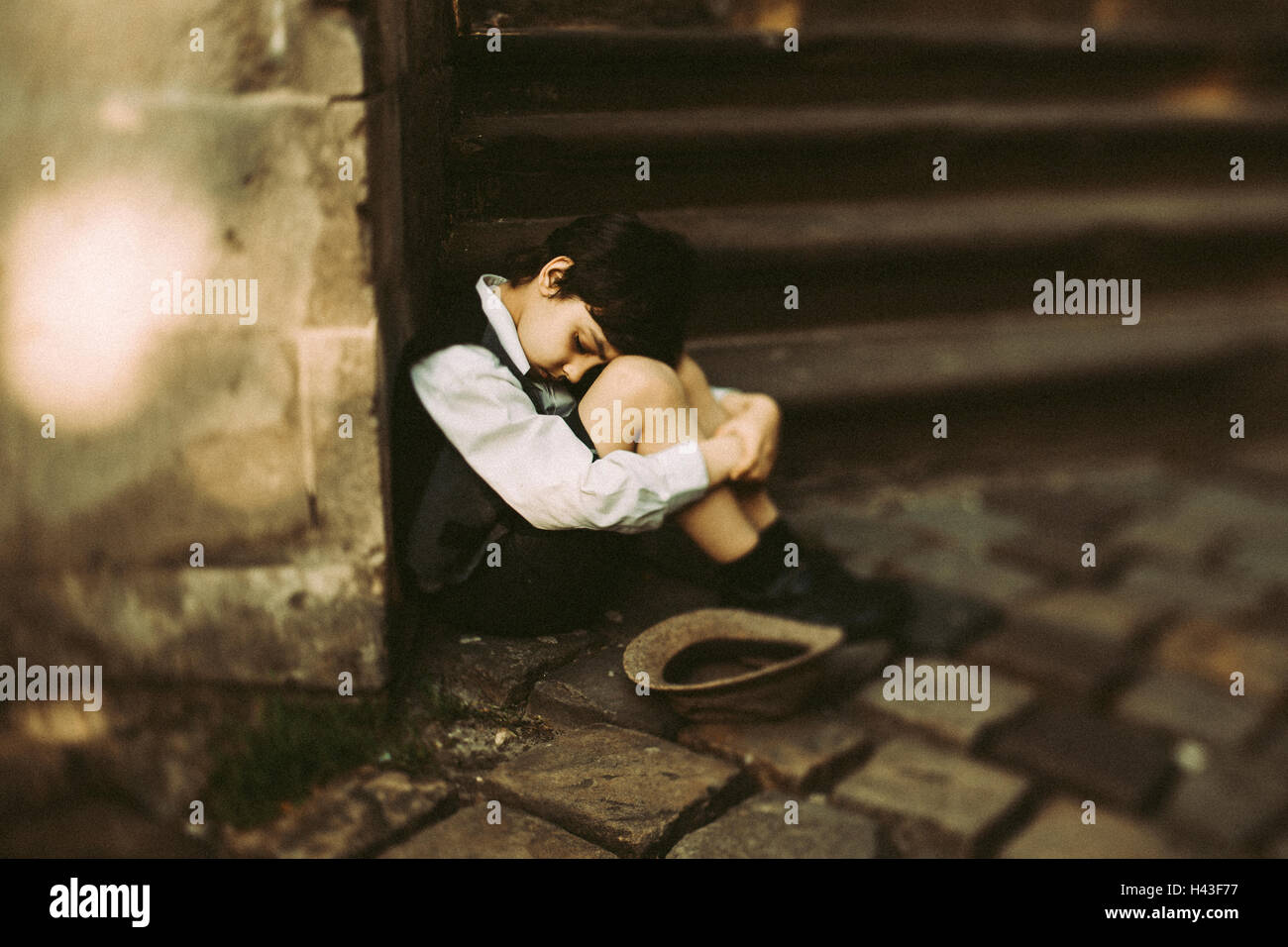 Old-fashioned Caucasian boy sitting near staircase begging for money Stock Photo