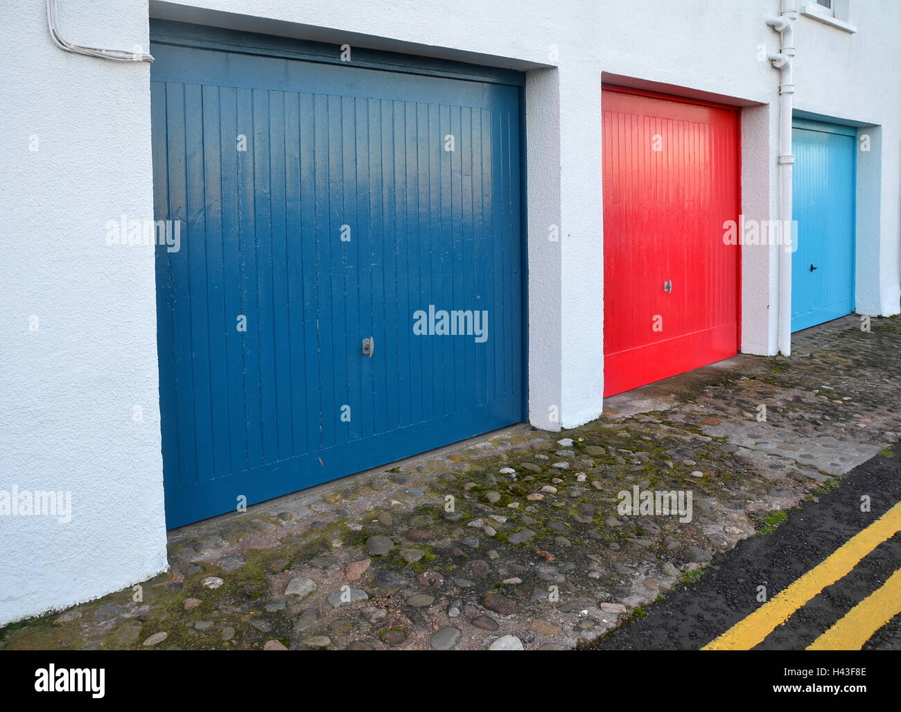 A row of red, blue, and pale blue garage doors run parallel with double yellow lines painted on the roads edge. Stock Photo
