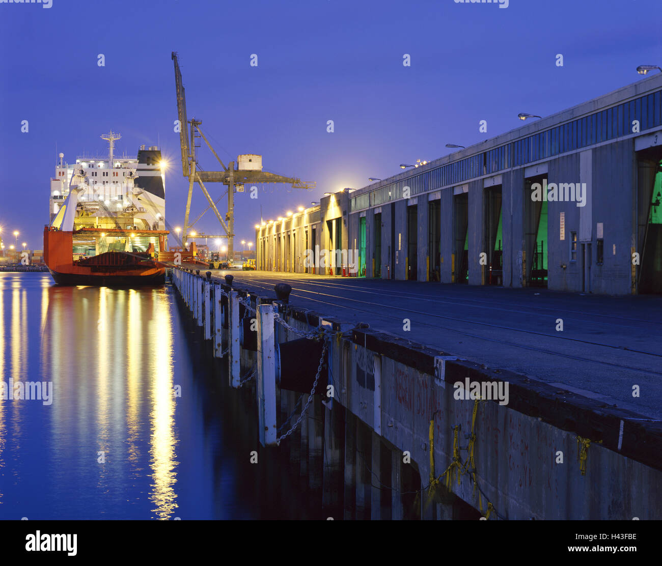 Cargo ship under crane in harbor at night Stock Photo