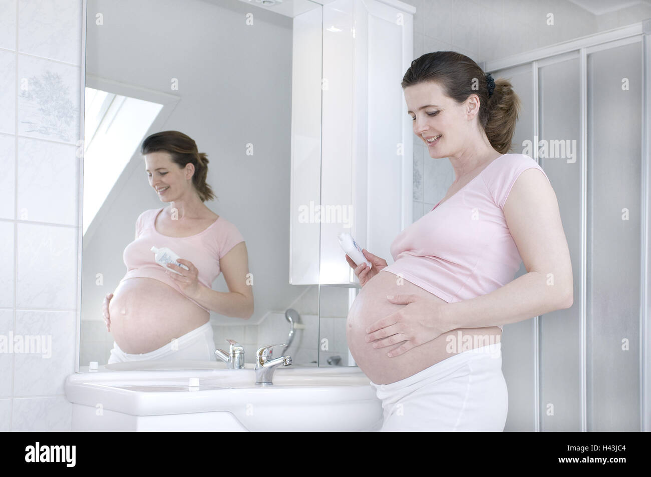Woman, young, pregnant, bathrooms, stand, lubricate abdomen, side view, model released, Stock Photo