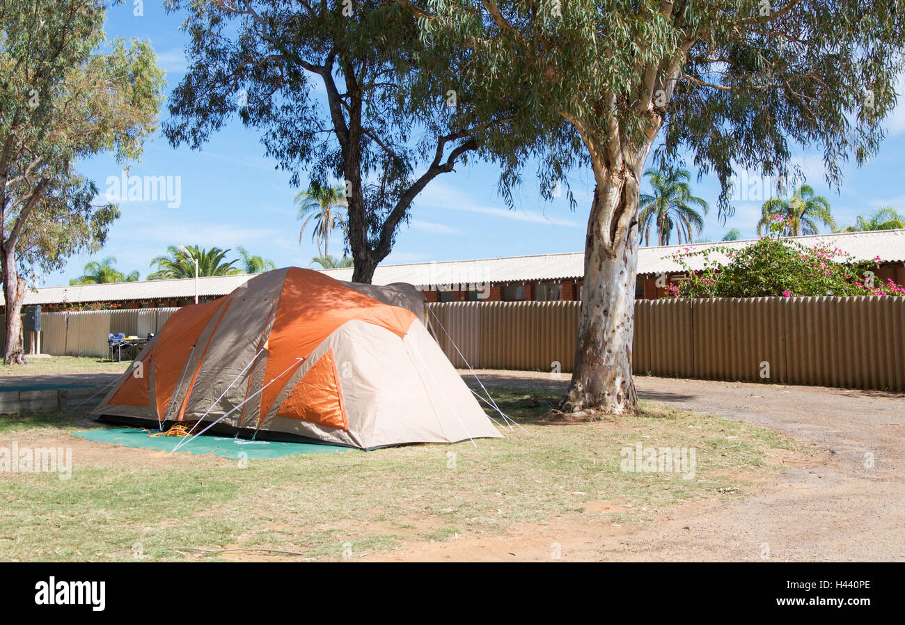 Assembled tan and orange camping tent on tarp in grass and treed