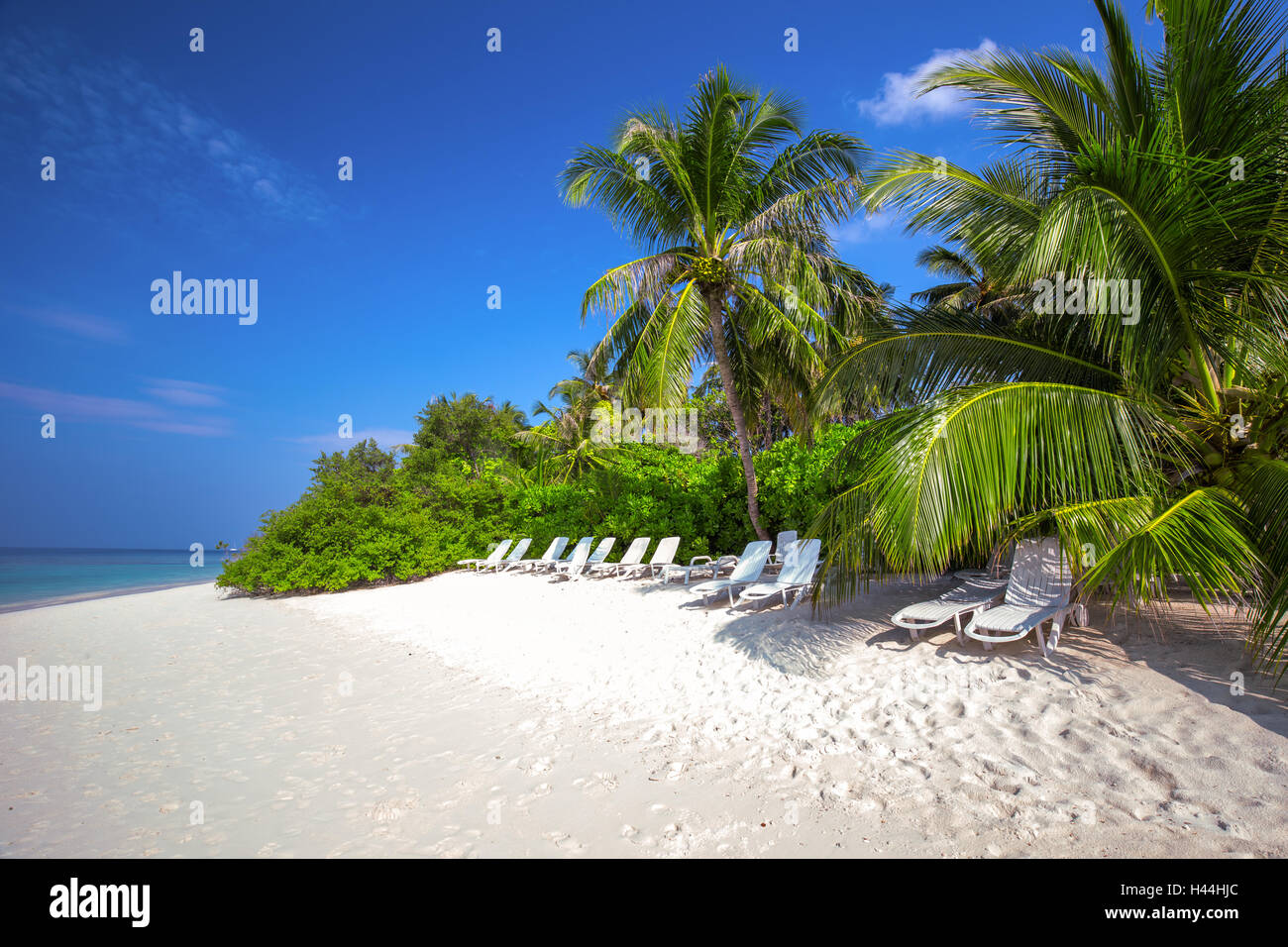 Tropical Maldives island with sandy beach, palm trees, overwater bungalows and tourquise clear water Stock Photo