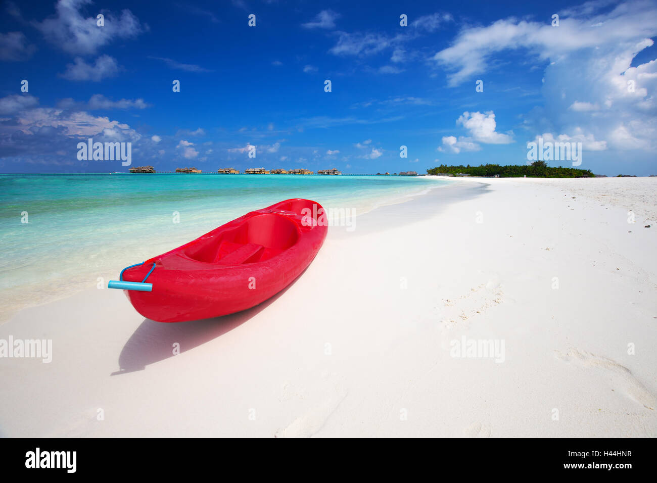 Red kayak on tropic beach with palm trees and overwater bungalows Stock Photo