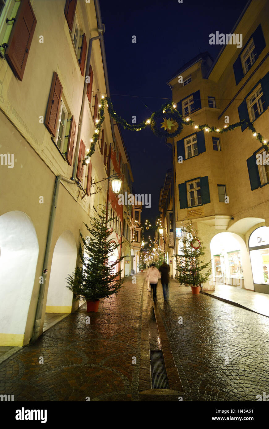 Italy, South Tyrol, Merano, bower lane, for Christmas, passers-by, evening, town, town view, pedestrian area, lane, Advent, yule tide, Christmas, Advent decoration, decoration, Christmas decoration, Christmas trees, shops, shops, shop-windows, houses, arcades, illuminateds, cobblestones, person, couple, back view, stroll, winter, lanterns, night, Stock Photo