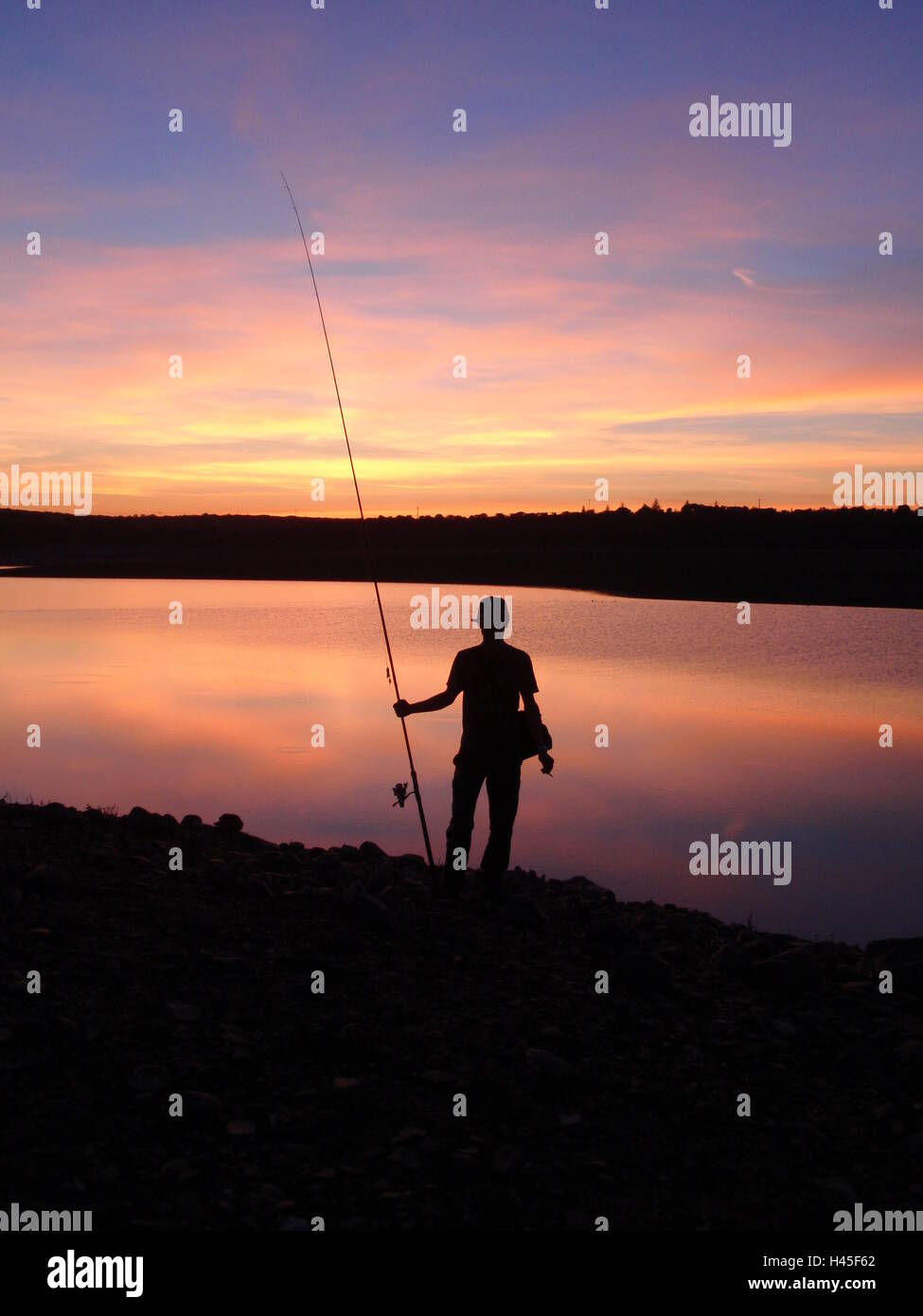 Fisherman silhouette on sunset on a lake Stock Photo - Alamy