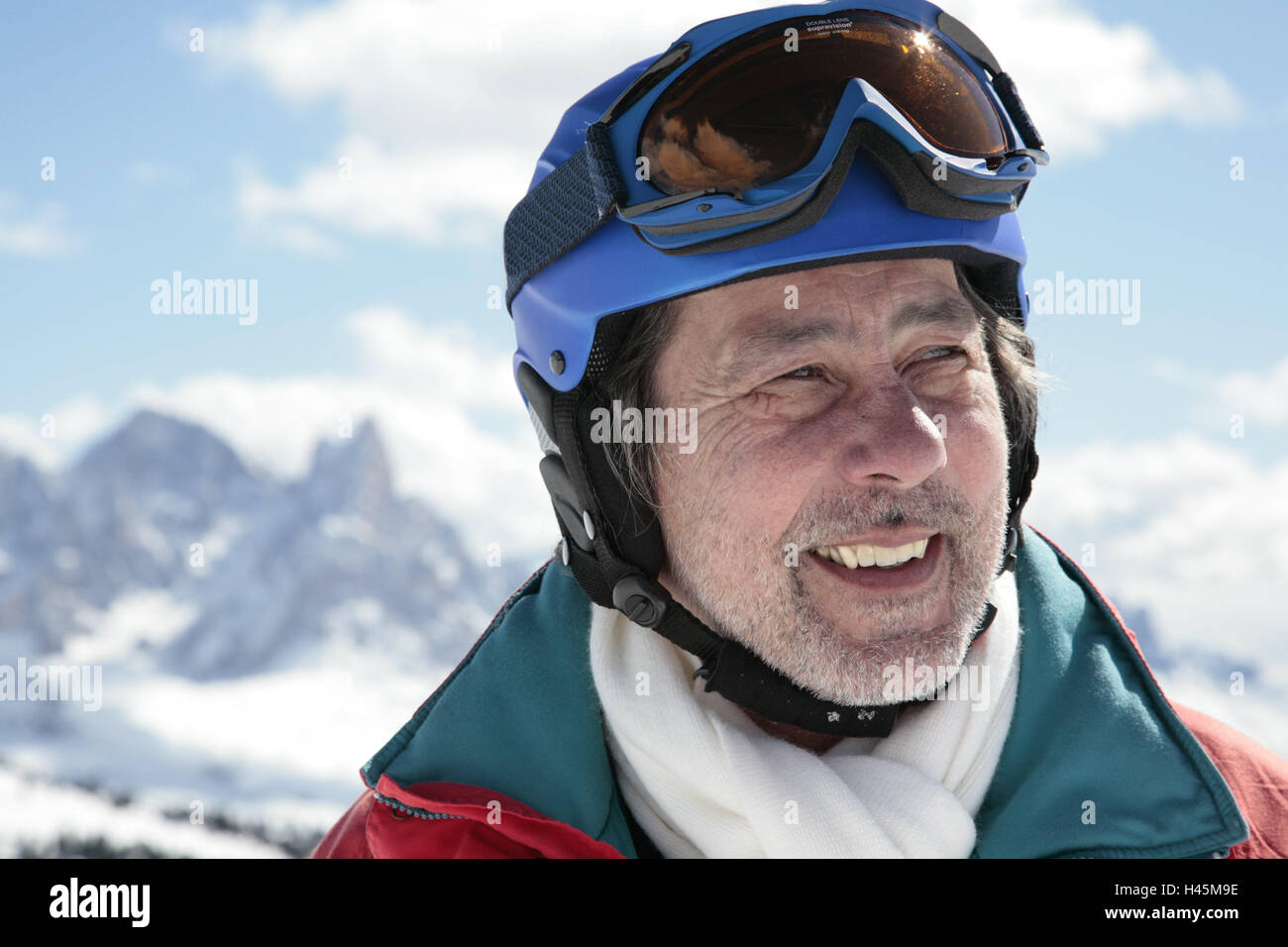 Italy, the Dolomites, Fassatal, senior, ski helmet, smile, portrait, curled, background, mountains, mountain world, snow-covered, veil clouds, man, person, stand, view, side view, ski glasses, beard, anorak, ski jacket, scarf, vacation, leisure time, recreation, joy, perseverance, sport, winter sports, skiing, mountain air, helmet, accident prevention, protection, Stock Photo