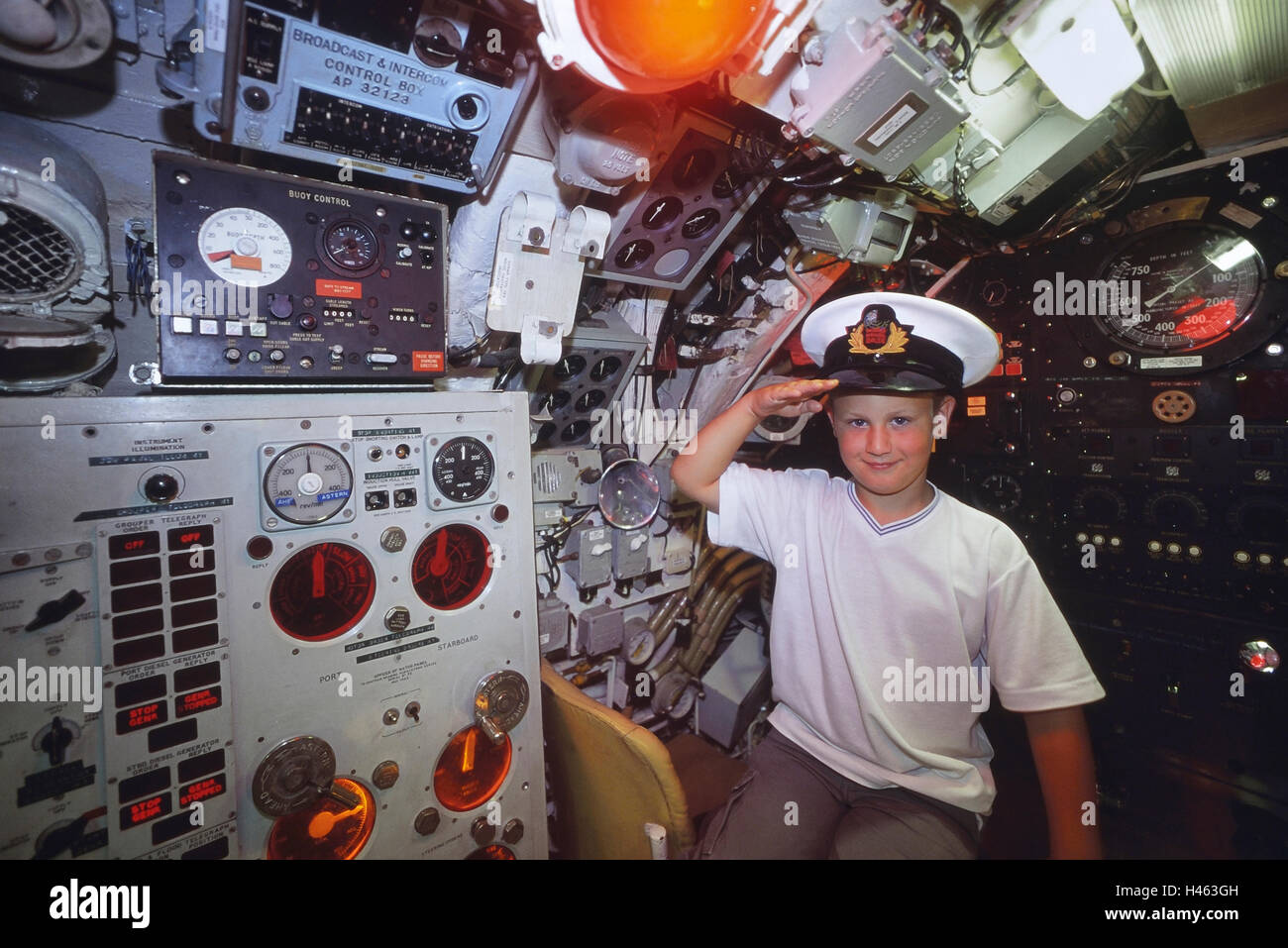 Young boy wearing a Navy officer peak cap saluting from the Helm of the Pilot's station onboard Oberon class submarine HMS Ocelot. HM Submarine Ocelot Stock Photo