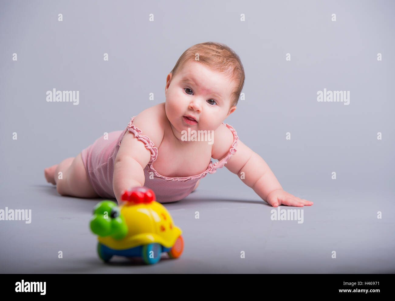 cute baby girl crawling on a gray floor, playing with a colorful toy Stock Photo