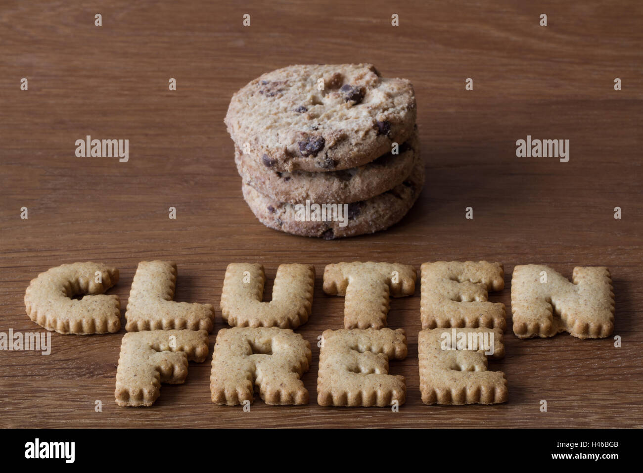 The food advice 'Gluten Free' spelled with alphabet shaped cookies alongside a stack of chocolate chip biscuits on wood. Stock Photo