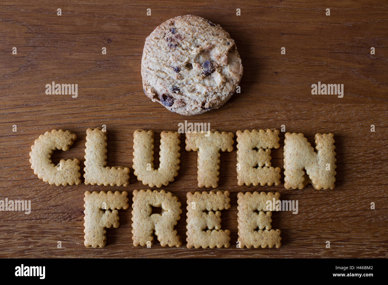 The food advice 'Gluten Free' spelled with alphabet shaped cookies alongside a stack of chocolate chip biscuits on wood. Stock Photo