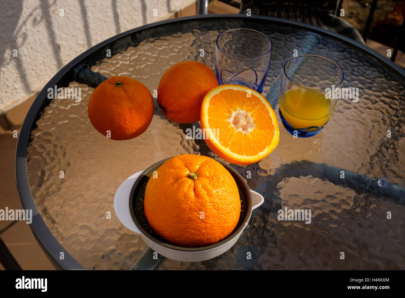 orange juicer glasses and cut orange on a glass table outside without H46K0M