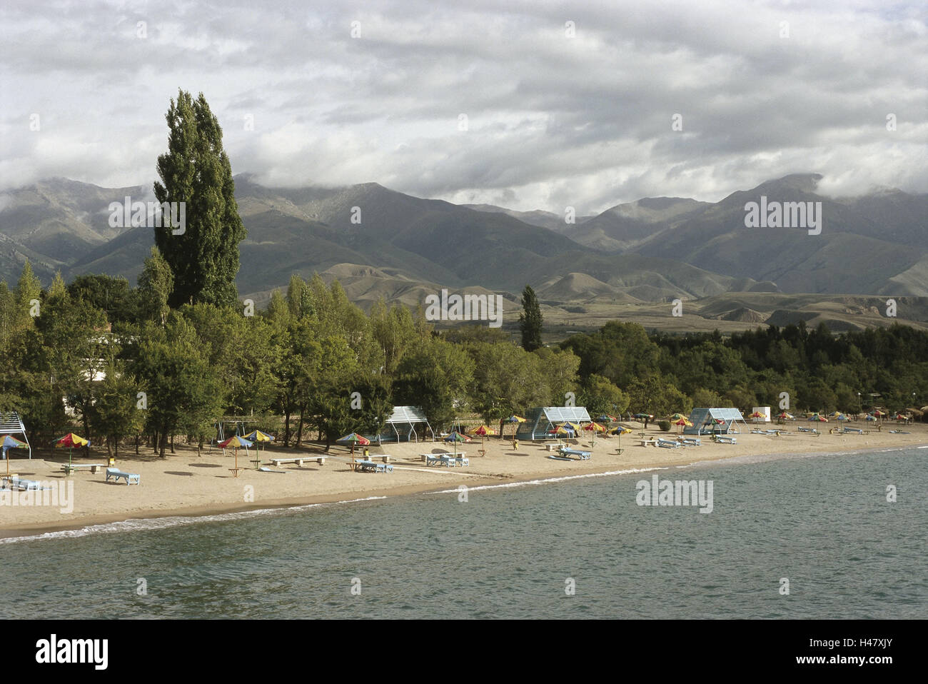 Kirghizistan, lake Yssykköl, hotel beach, overview, scenery, summer, cloudy sky, Asia, Central Asia, Central Asia, waters, Issyk-Kul, Bulan-Sogottu, shore, lakeside, north shore, sandy beach, beach scene, beach, Sand, display screens, sun benches, beach lying, lying, sunshades, trees, wood, hinterland, mountains, mountain landscape, vacation, leisure time, summer vacation, beach holiday, beach vacation, destination, person, rest, recreation, Stock Photo