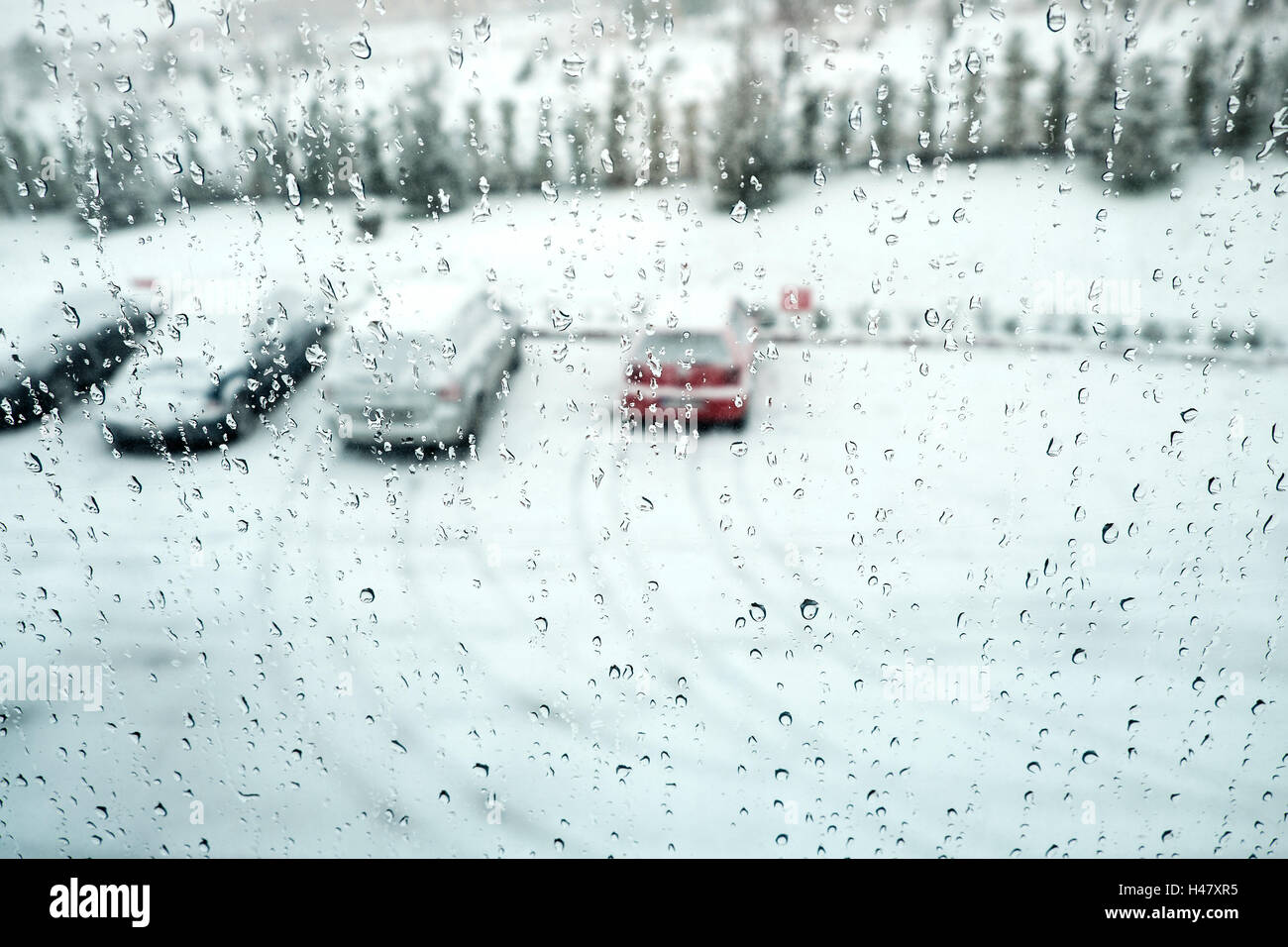 A view of parked cars at the snowy and rainy day from behind the window