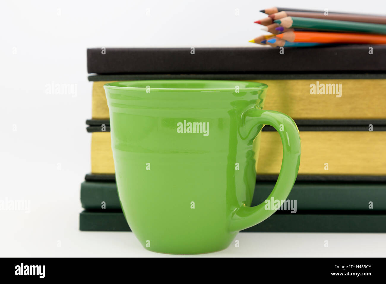 Green mug in front of books with colored pencils on top reflect alert attention to academic study and intellectual work. Stock Photo