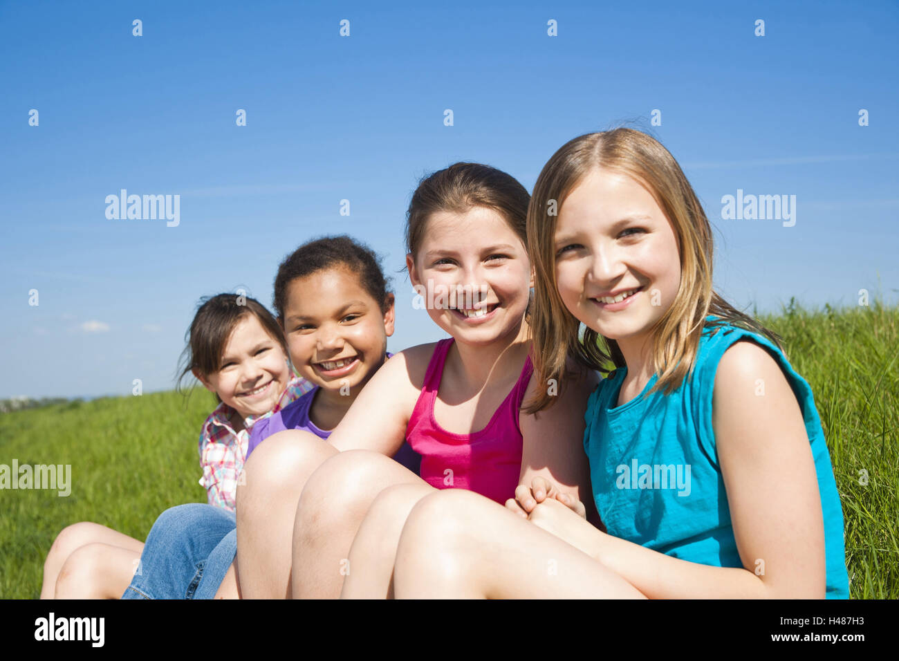four girls sit happily on a meadow, Stock Photo