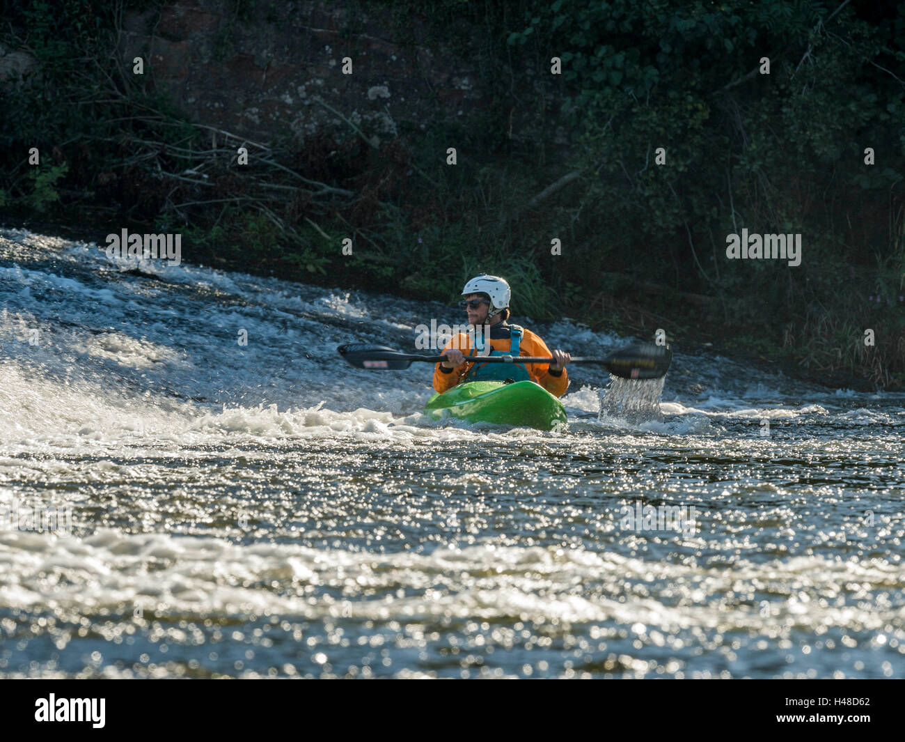 Male adult White Water Kayaking along a River Exe Weir on a bright