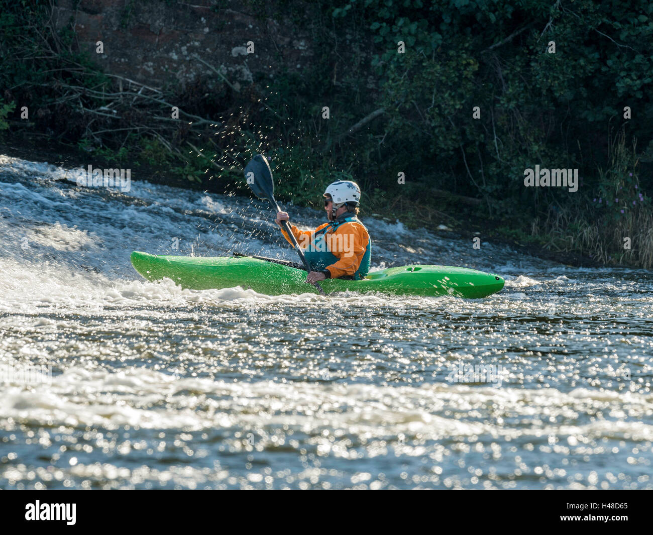 Male adult White Water Kayaking along a River Exe Weir on a bright