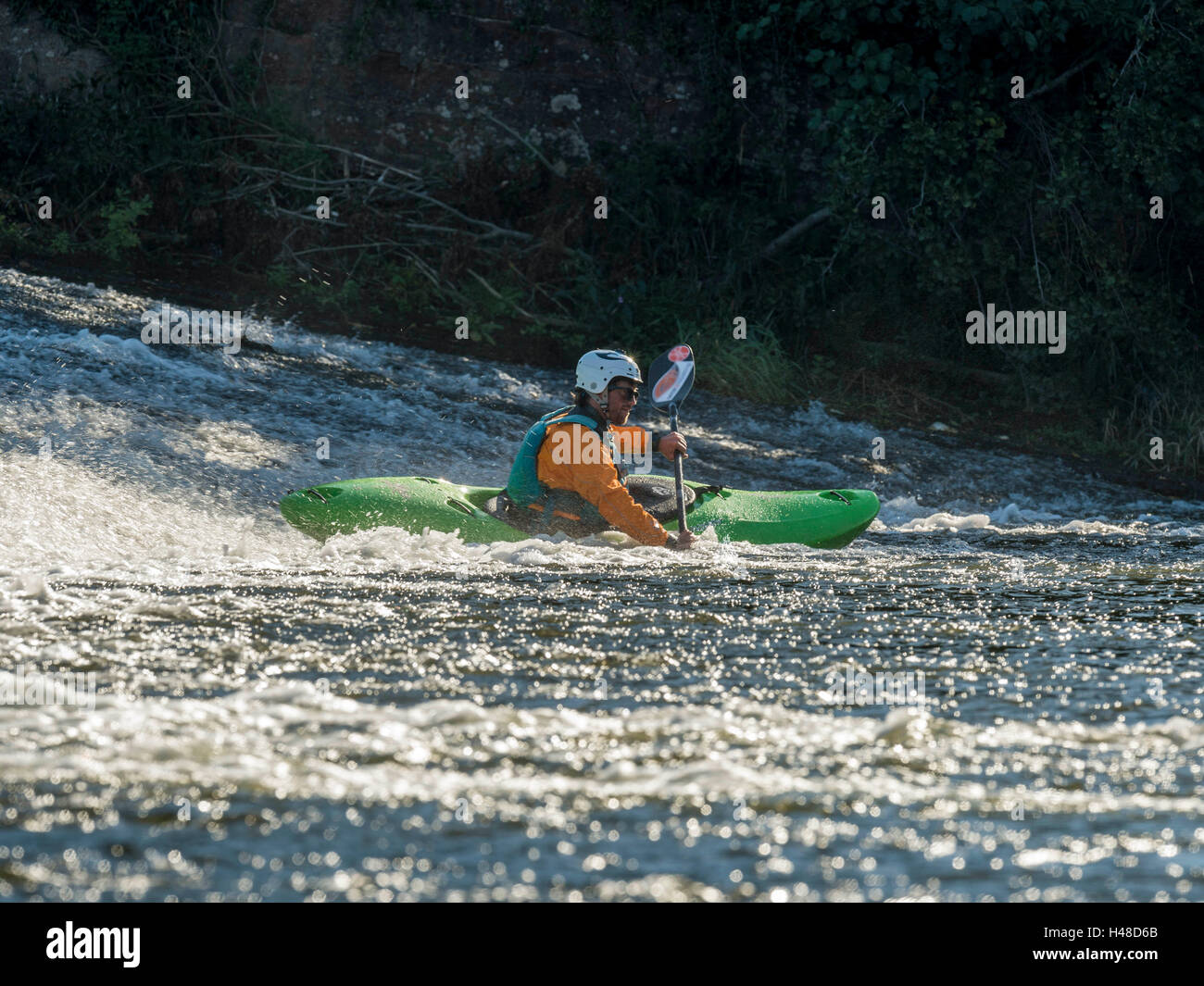 Male adult White Water Kayaking along a River Exe Weir on a bright Autumn day. Situated near Exeter in Devon, United Kingdom Stock Photo