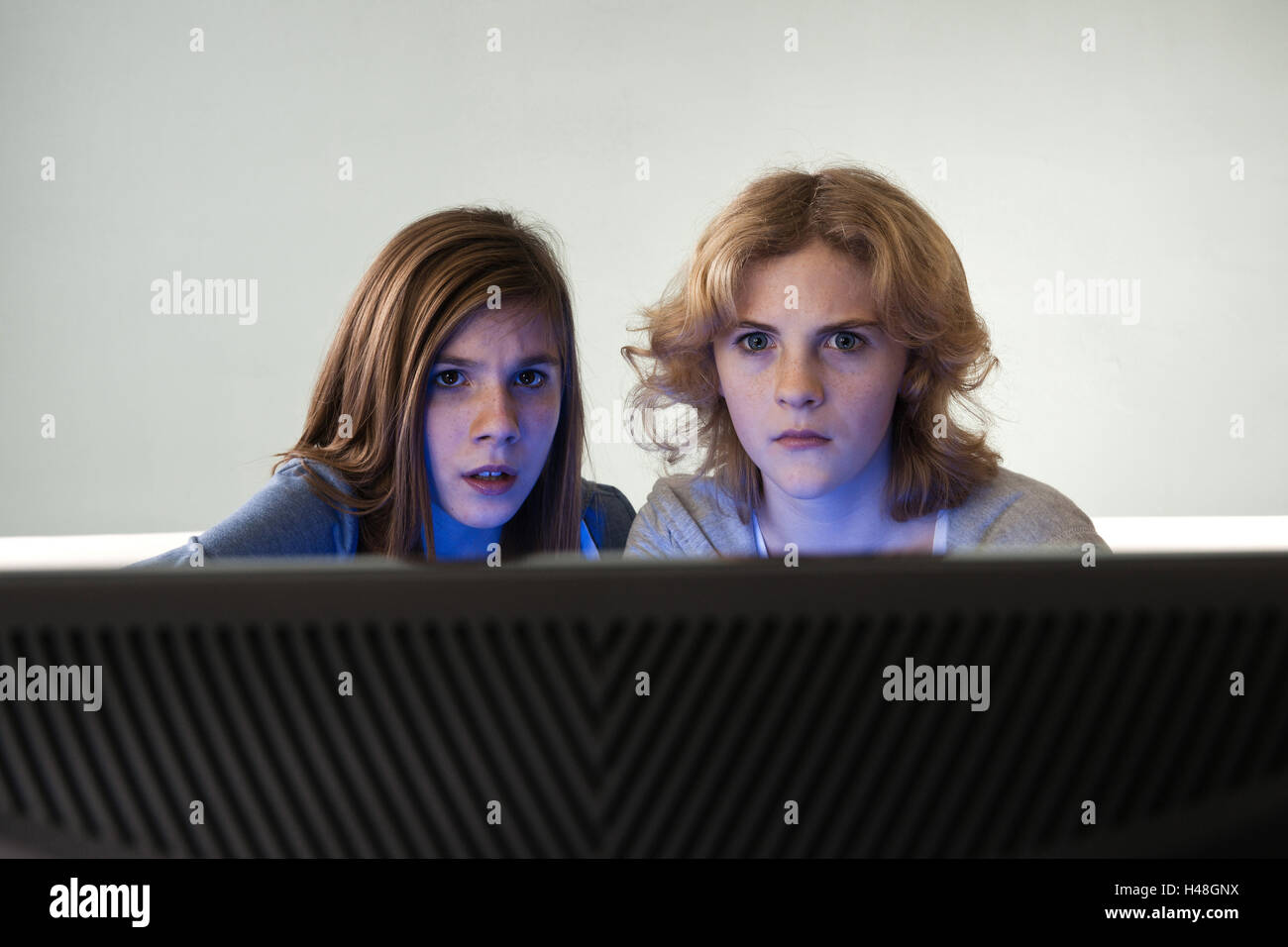 Two girls sit anxiously before a TV, Stock Photo