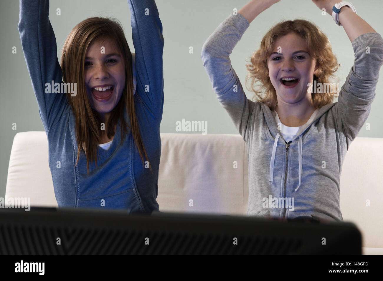 Two girls sit rejoicing before a TV, Stock Photo