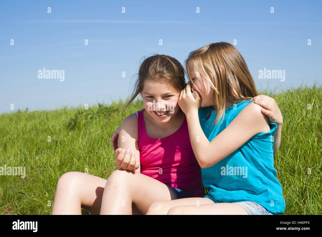 two girls sit arm in arm on a meadow, whisper, secret Stock Photo - Alamy