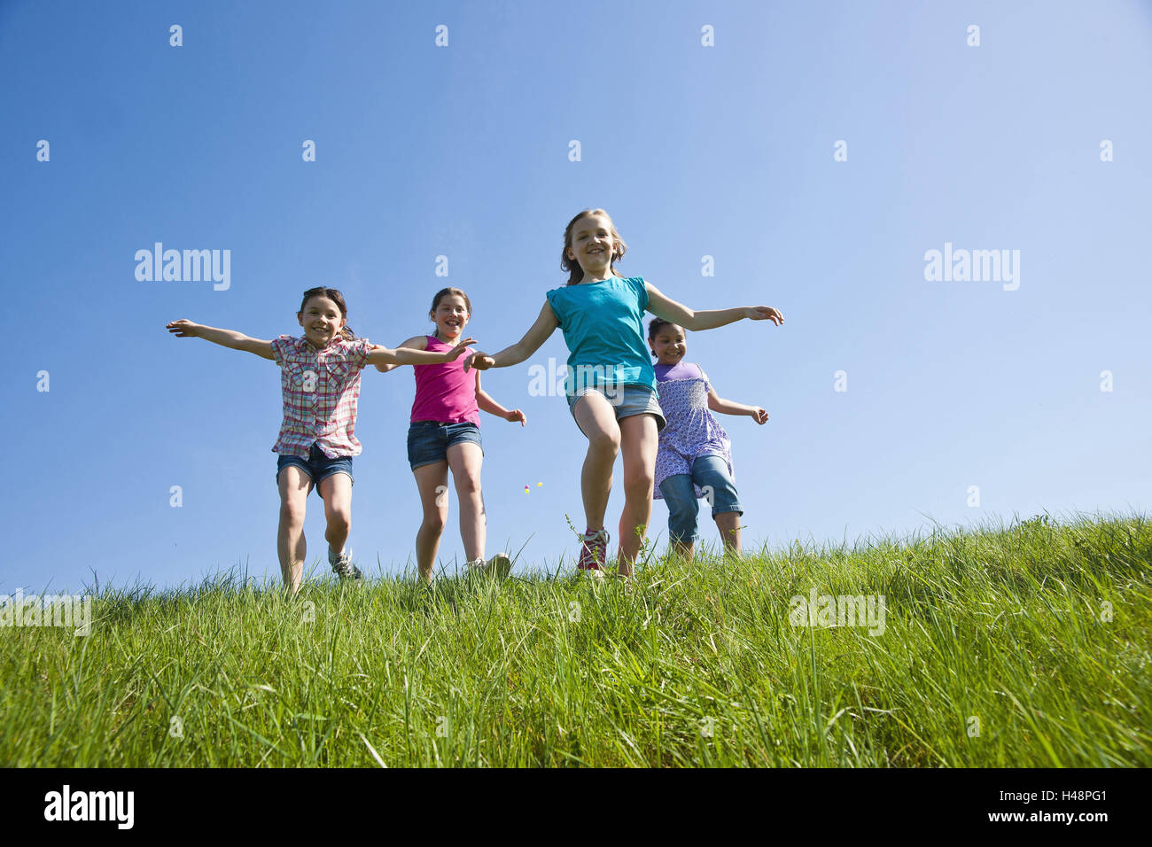 four girls run happily above a meadow, Stock Photo