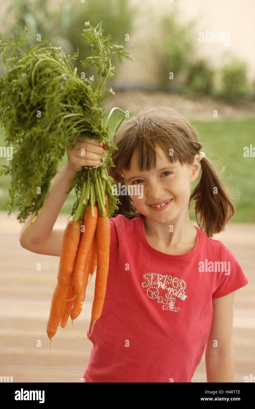 Child, girl, carrot bundle, hold, smile, outside, view camera, half portrait, Stock Photo