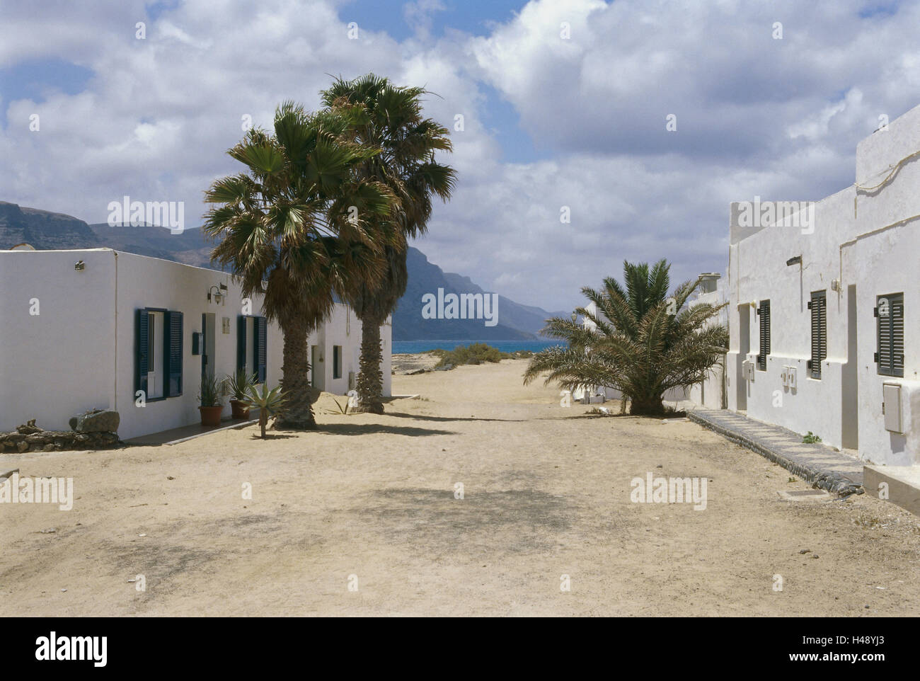 Spain, the Canaries, island La Graciosa, Caleta del Sebo, Dorfstrasse, houses, palms, architecture, street, dusty, heat, wilderness, defensive wall, clouds, heavens, residential houses, exit, outside, deserted, Stock Photo