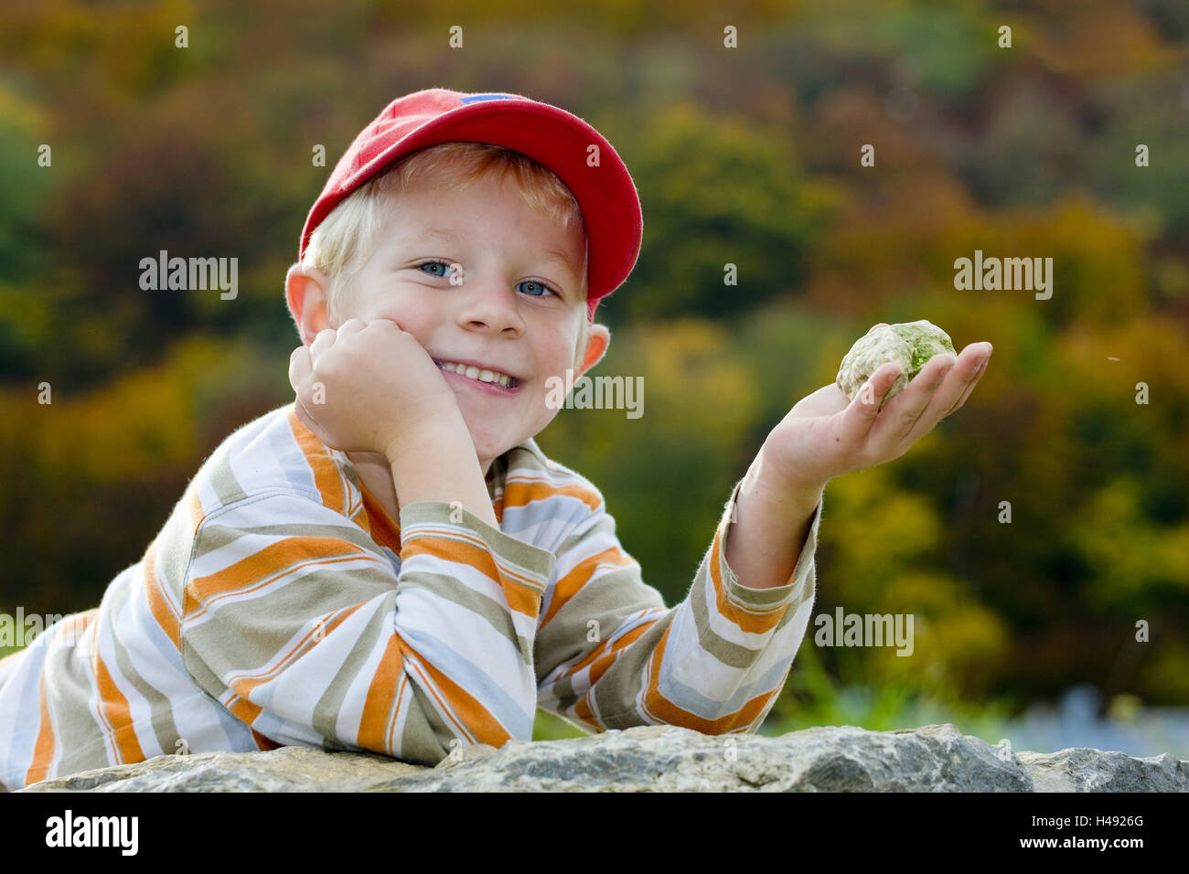 Boy, sign cap, hand, stone, hold, smile, portrait, model released, people, child, blond, head, rock, hand, add support, leisure time, collect, point, cap, baseball cap, red, autumnally, nature, Stock Photo