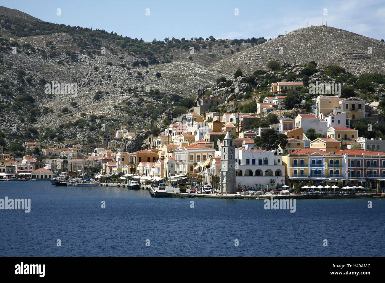 Greece, Dodekanes, Rhodes, island, Symi, harbour place Gialos, town view, promenade, clock tower, hill, sea, coast, seashore, coastal place, local view, Simi, town, island capital, mountains, Symi town, houses, harbour, tower, architecture, boots, ships, bank promenade, harbour promenade, street cafe, place of interest, holiday resort, Stock Photo