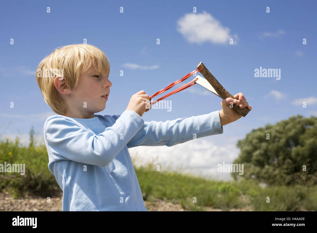 Young, slingshot, aim, sidewise, half portrait, people, child, blond, blue, outside, alone, target, focussed, unerring, slingshot, weapon, rubber, courage, determination, targetting, focus, stretch, shoot, play, Stock Photo
