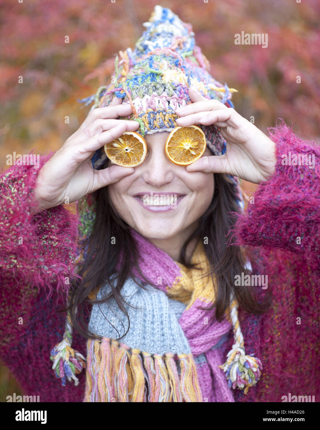 Woman with cardigan, cap and scarf holds slices of orange before the eyes, portrait, Stock Photo