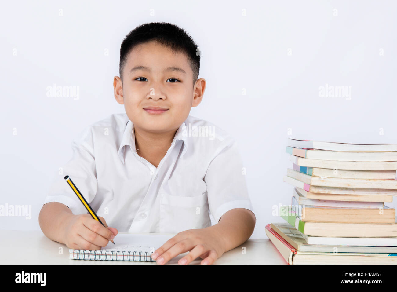 Asian Chinese Little Boy Wearing Student Uniform Writting Homework in plain isolated white background. Stock Photo