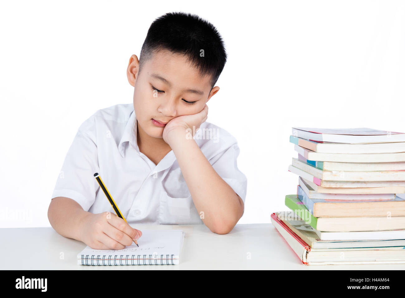 Bored Asian Chinese Little Boy Wearing Student Uniform Writting Homework in plain isolated white background. Stock Photo