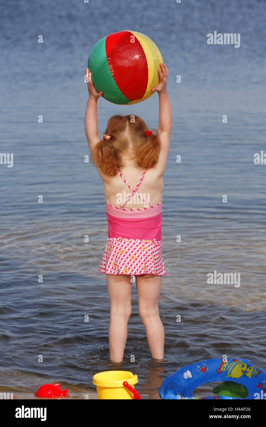 Girls with toys in the water, ball hold up, back view, Stock Photo