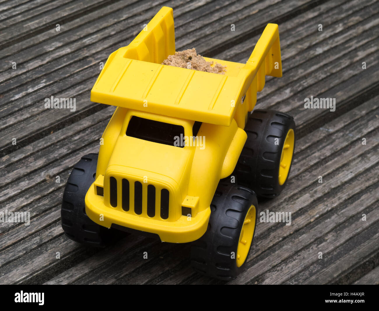 Toy dump truck - Yellow plastic with load of sand on brown wooden background Stock Photo