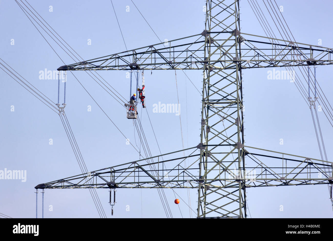 High-voltage pole, lines, man climbing to side arm, other man working in gondola, Thuringian Forest Stock Photo