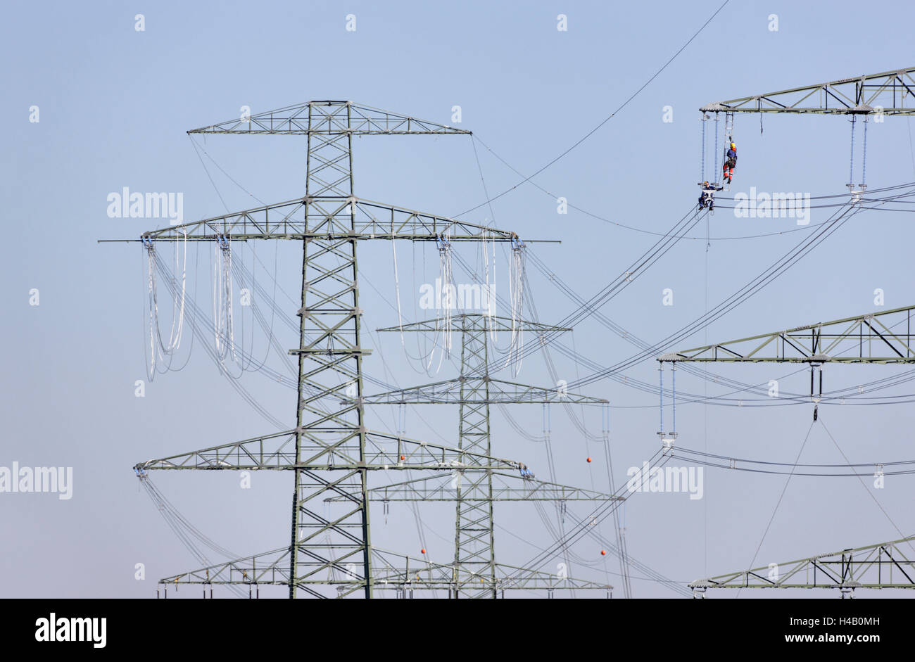 High-voltage poles, wires, power line installation, power supply lines, man sitting on power lines, other man climbing to side arm, Thuringian Forest Stock Photo