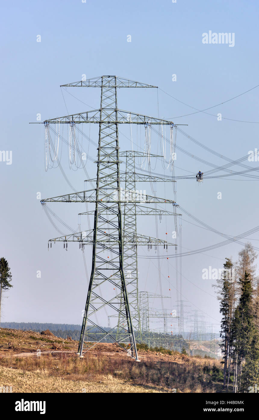 High-voltage poles, wires, man working on power line installation, gondola, wood, swath, Thuringian Forest Stock Photo