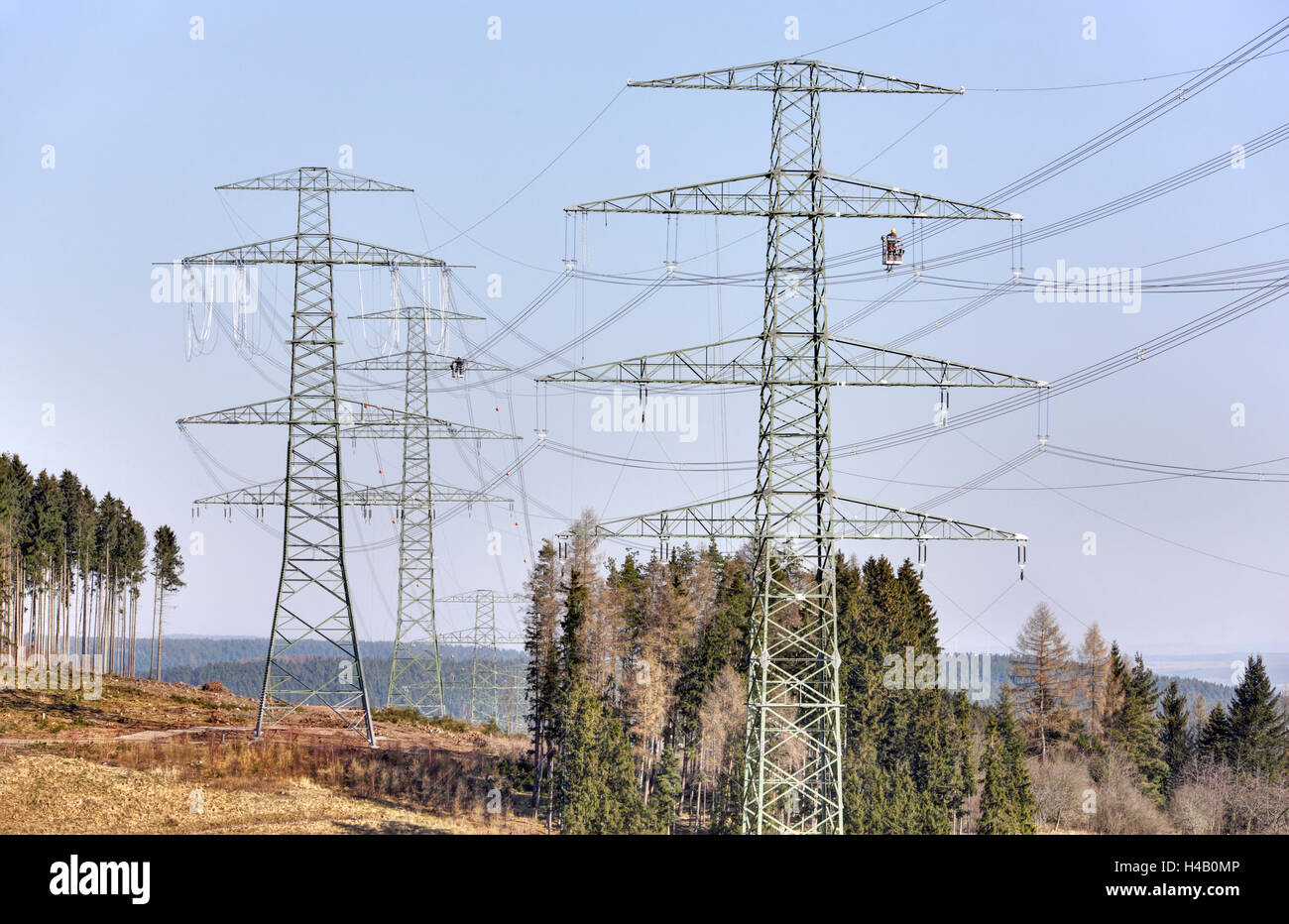 High-voltage poles, wires, two men working on power line installation, gondolas, forest, swath, Thuringian Forest Stock Photo