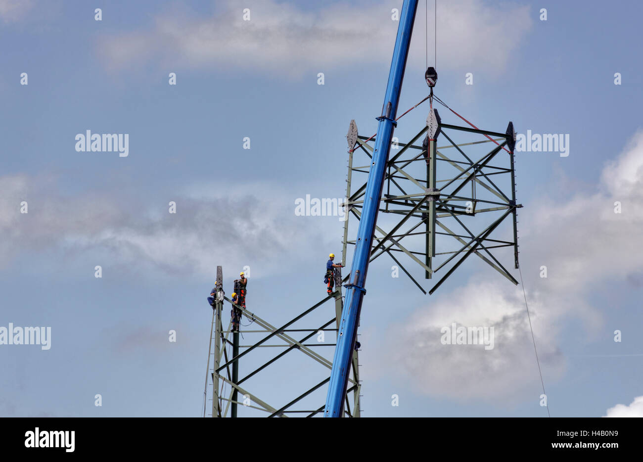 Men working in the high-voltage power pylon, crane raising part of the pylon, Thuringian Forest Stock Photo