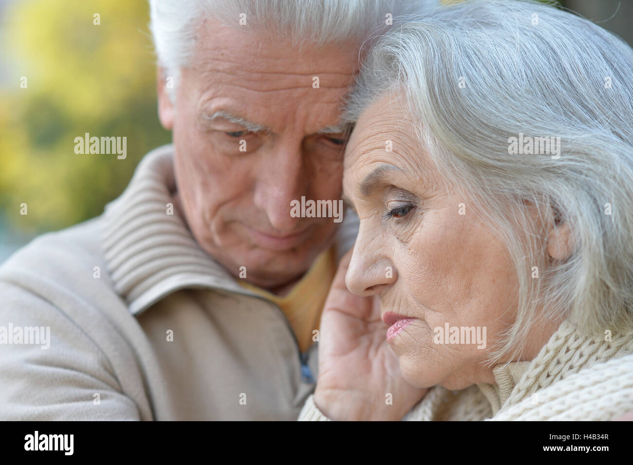 Sad elderly couple standing embracing outdoors Stock Photo