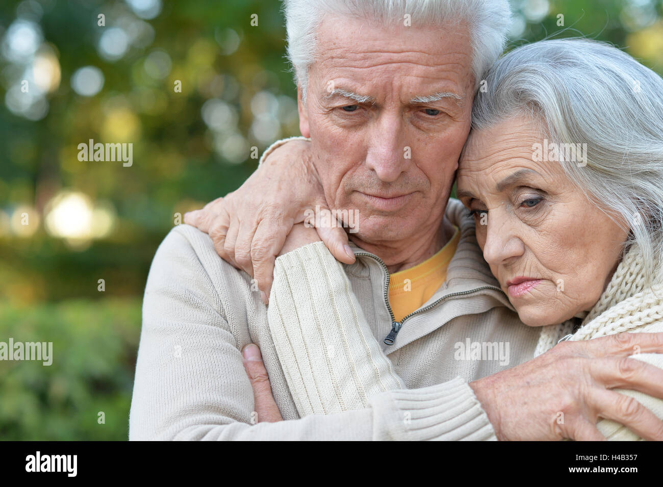 Sad elderly couple standing embracing outdoors Stock Photo