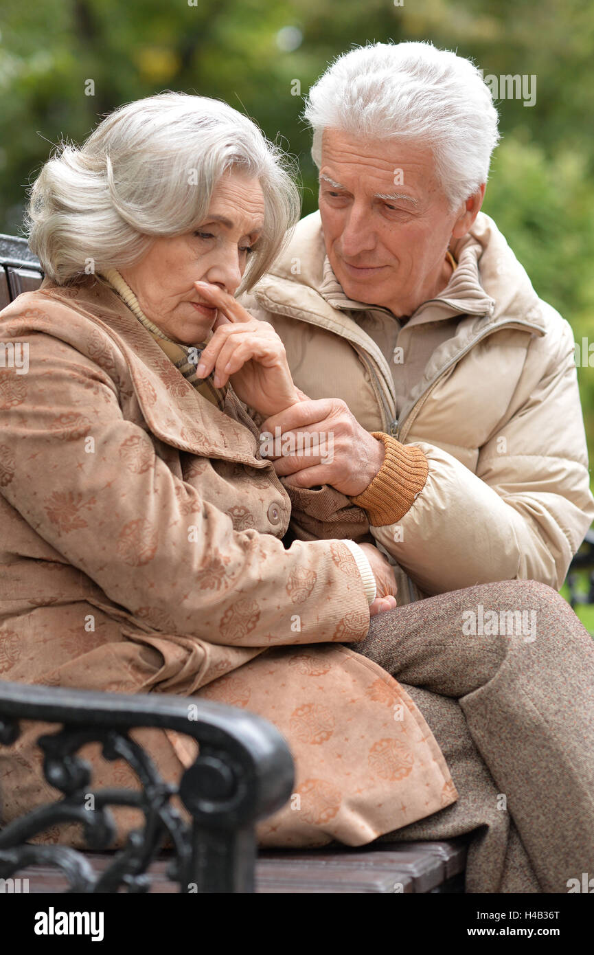 Sad elderly couple sitting on a bench in autumn park Stock Photo